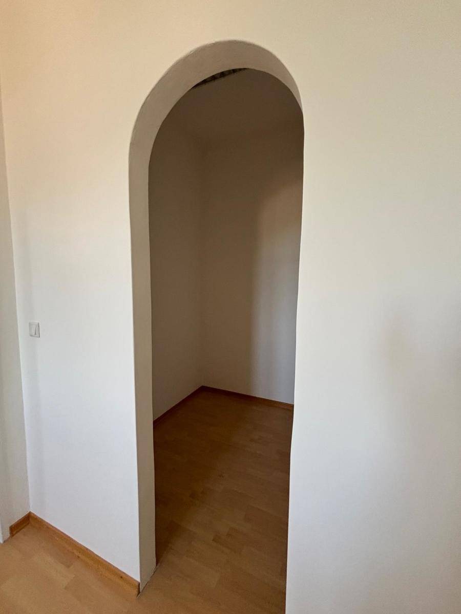 Kleiner, heller Raum mit Holzfußboden und Rundbogenzugang, ideal als Abstellkammer oder begehbarer Schrank.