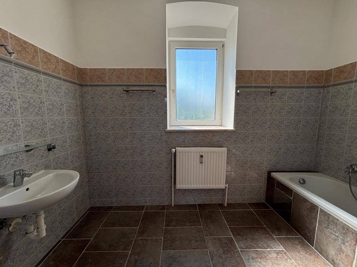 Badezimmer mit gemusterten Fliesen, Badewanne, Waschbecken und Fenster für Tageslicht.