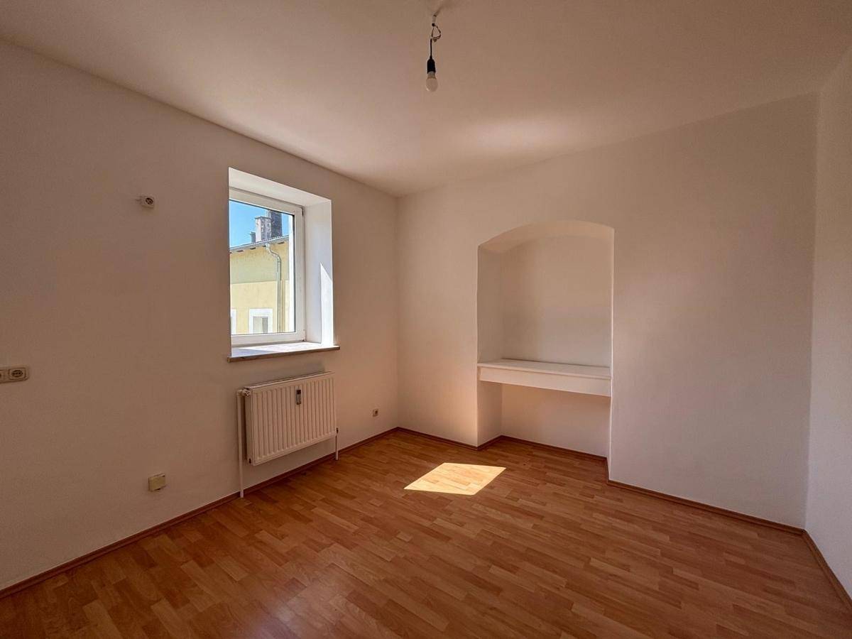 Helles Zimmer mit Holzfußboden, Fenster und einer praktischen Nische mit integrierter Ablage.