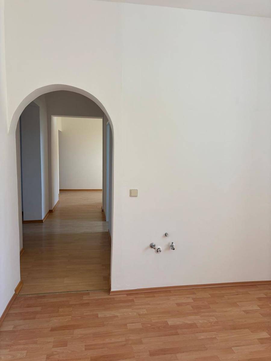 Raum mit Laminatboden und Rundbogen, vorbereitet für eine Küche mit sichtbaren Anschlüssen.