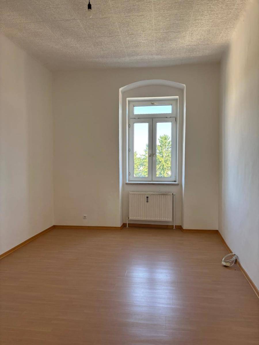 Geräumiges Zimmer mit Laminatboden, großem Fenster und Blick ins Grüne, ideal als Wohnbereich.