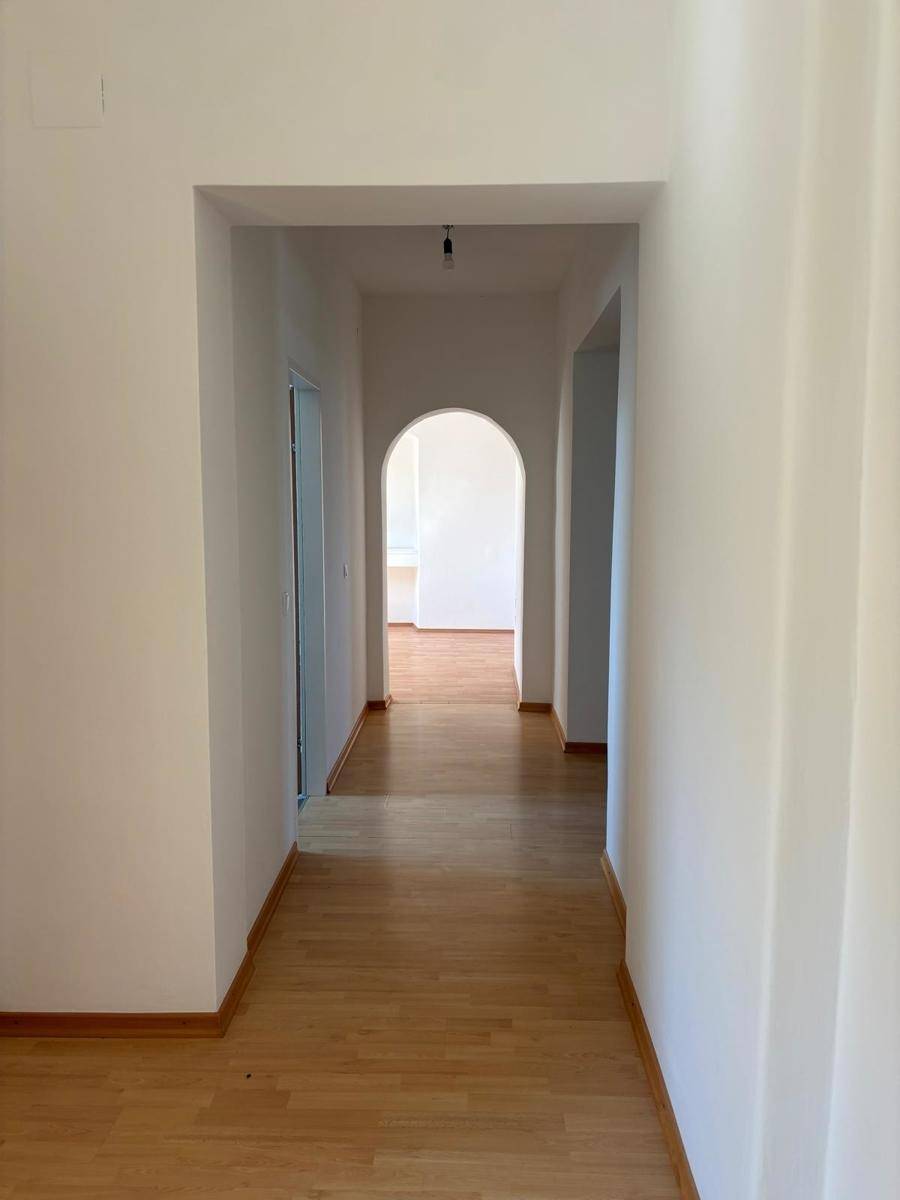 Langer, heller Flur mit Holzfußboden und einem eleganten Rundbogen, der die Räume verbindet.