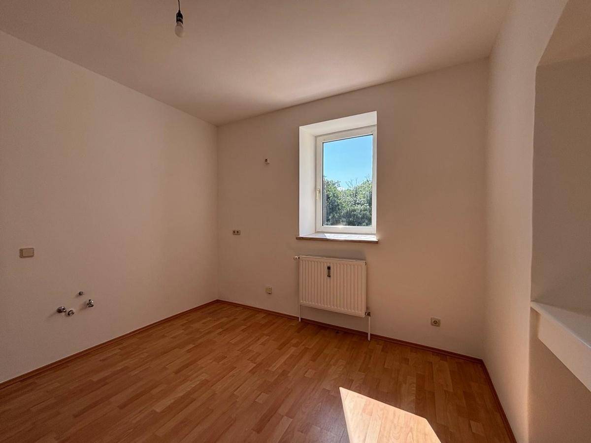 Leerer Raum mit Holzfußboden, Fenster und Heizkörper, bereit zur individuellen Gestaltung.