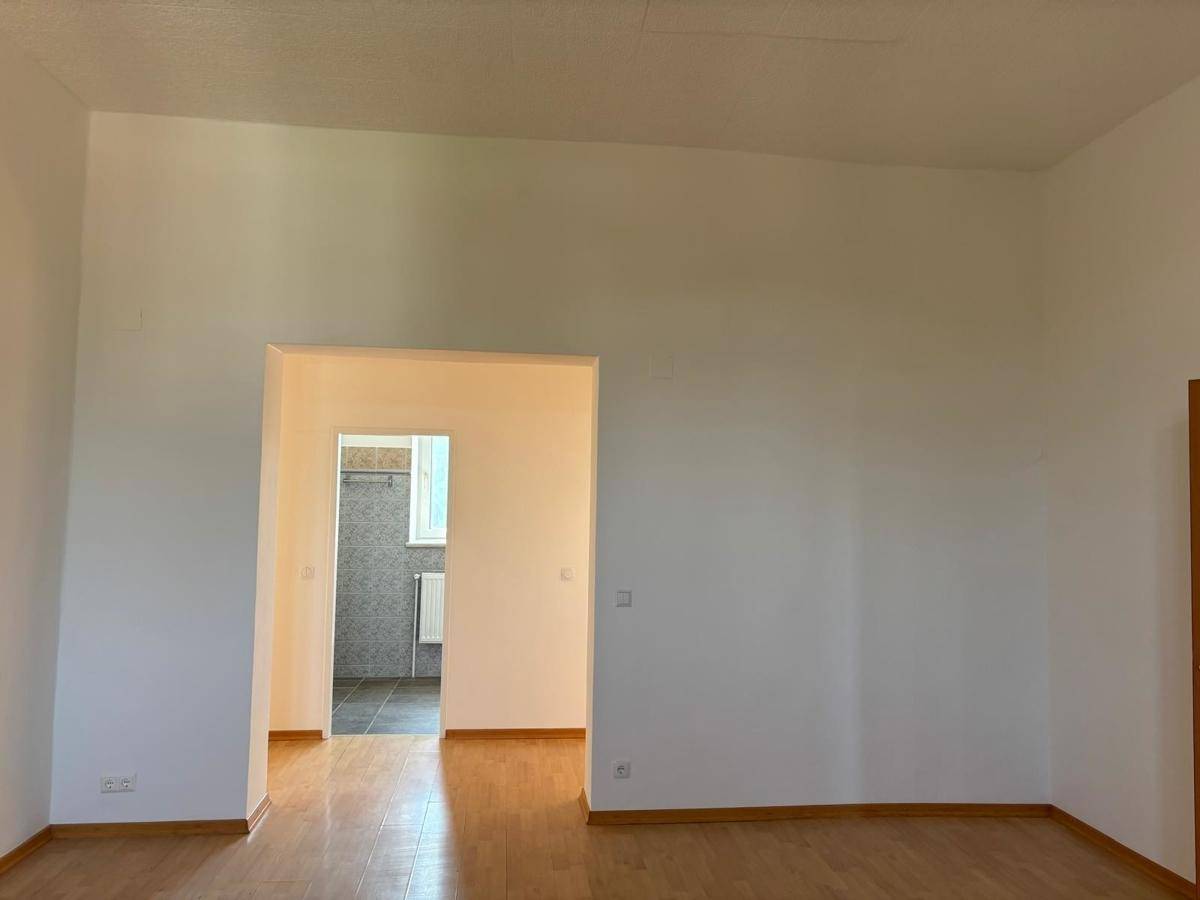 Heller Raum mit Laminatboden und zwei Türöffnungen, die zu angrenzenden Bereichen führen.