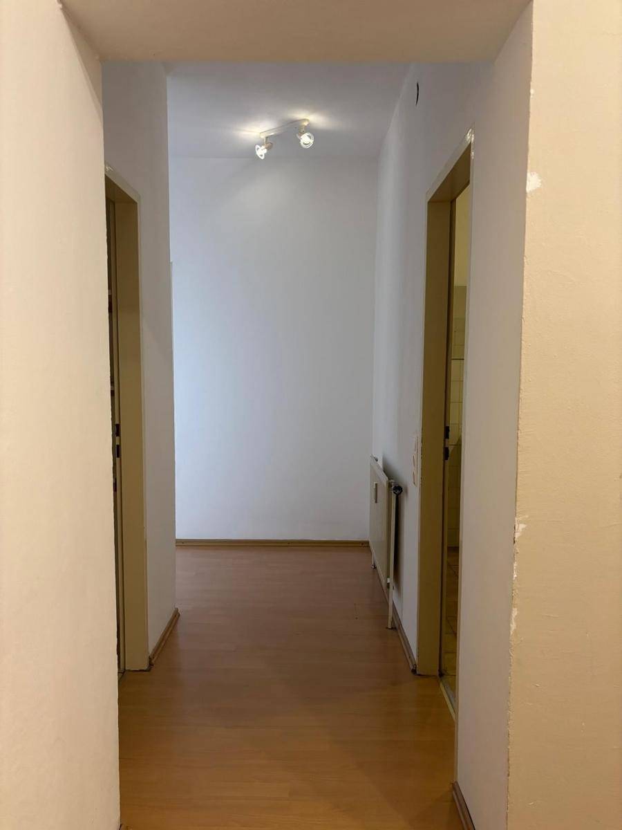 Langer Flur mit Laminatboden und Heizkörper, verbindet die verschiedenen Wohnbereiche der Wohnung.