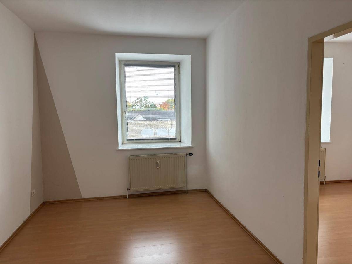 Gemütliches Zimmer mit einem Fenster, Heizkörper und Laminatboden, ideal als Schlaf- oder Arbeitszimmer.