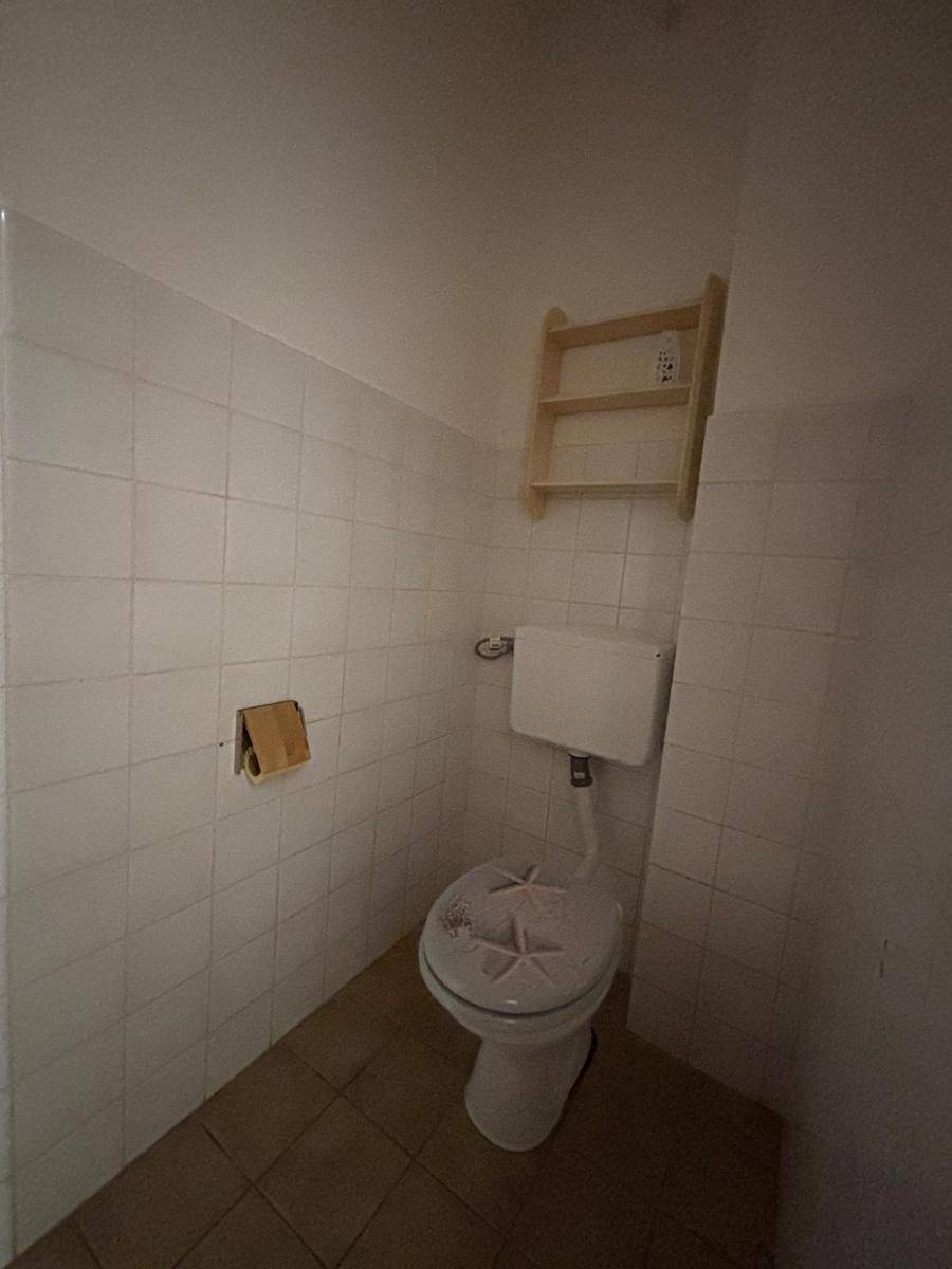 Separates WC mit Toilette und kleinem Regal, vollständig gefliest für einfache Pflege.