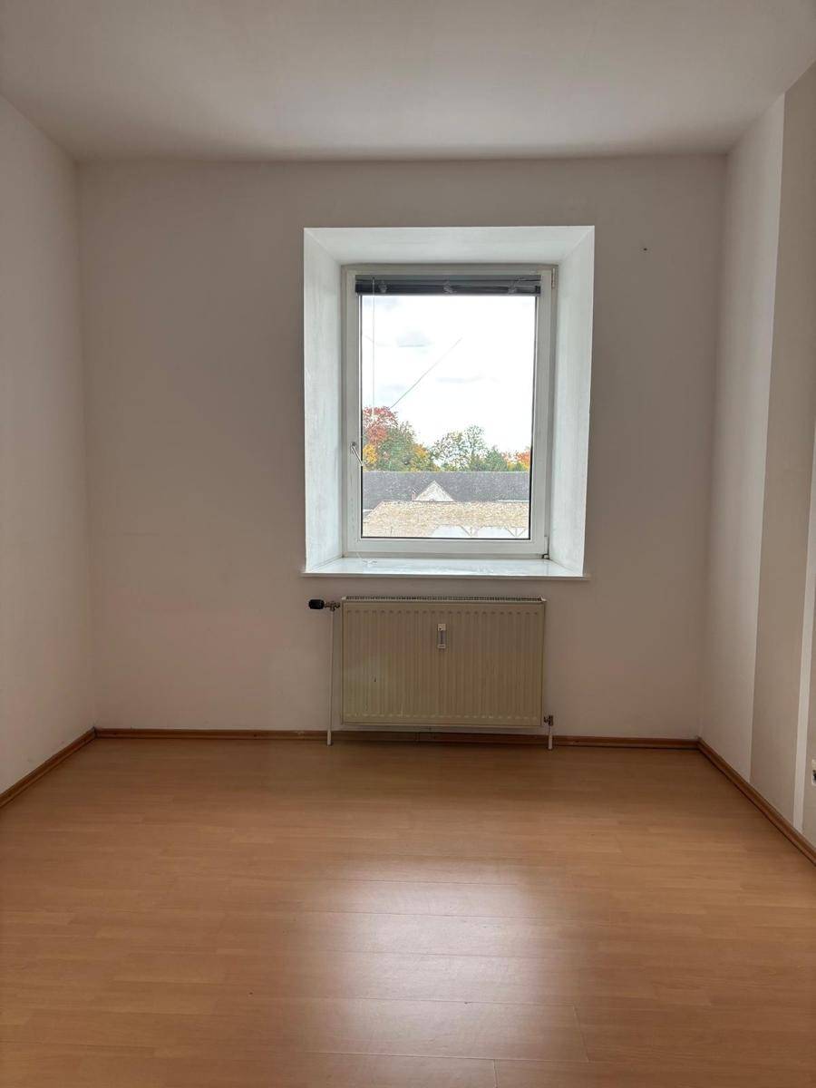 Geräumiges Zimmer mit großem Fenster, Heizkörper und Laminatboden, ideal für ein Schlafzimmer.