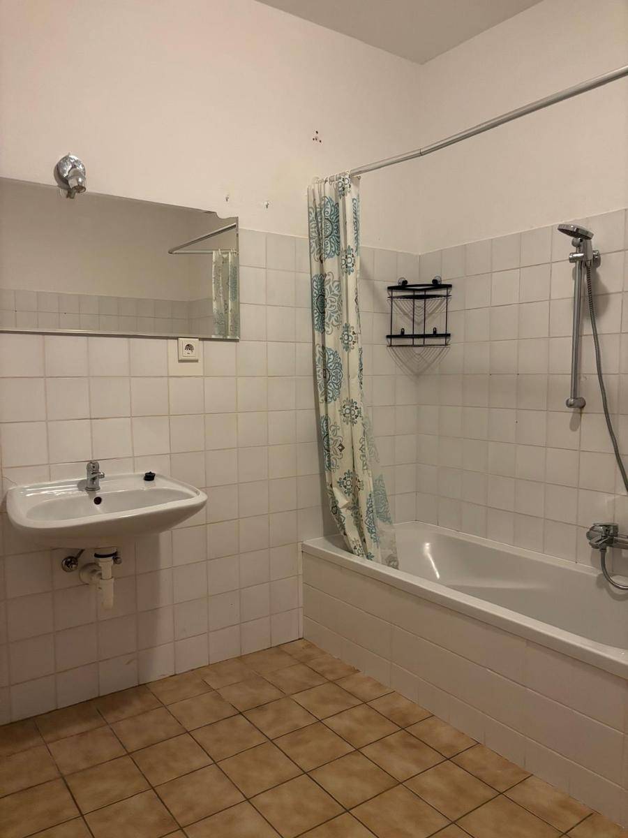 Badezimmer mit Waschbecken, Spiegel und Badewanne mit Duschvorhang, vollständig gefliest.