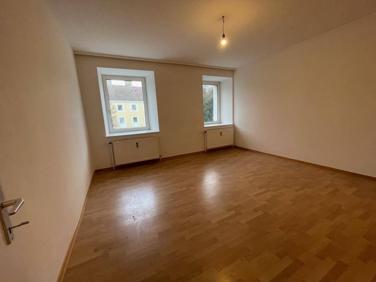 Helles Zimmer mit zwei Fenstern, Parkettboden und Blick ins Grüne.
