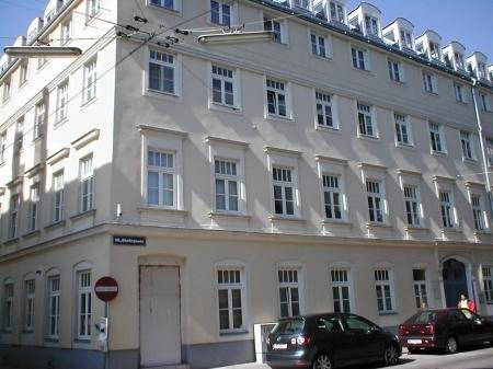 Eckgebäude mit klassischer Architektur, vielen Fenstern und Mansarddach in einer städtischen Umgebung.