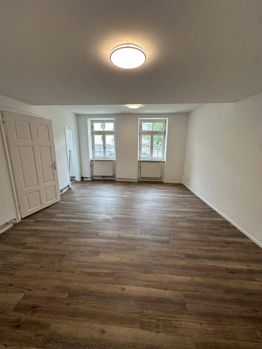 Geräumiger, leerer Raum mit neuem Laminatboden, weißen Wänden und zwei Fenstern.