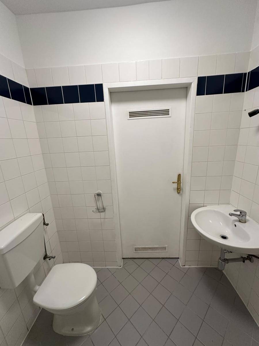 Kleines Badezimmer mit WC, Waschbecken und weiß-blauen Wandfliesen.