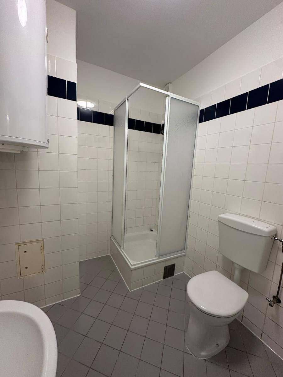 Badezimmer mit Duschkabine, WC und weiß-blauen Fliesen an den Wänden.