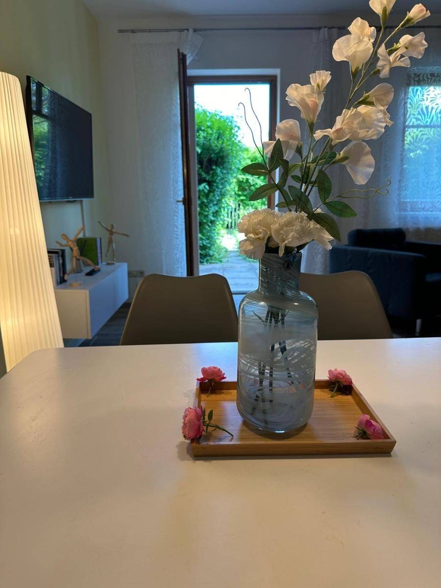 Detailansicht des Esstisches mit Blumenvase und Blick auf den Garten durch die offene Tür.