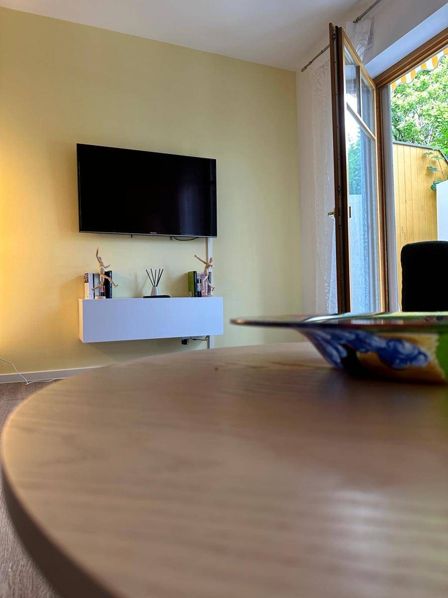 Wohnzimmer mit Couchtisch, Fernseher an der Wand und einem dekorativen Element im Vordergrund.