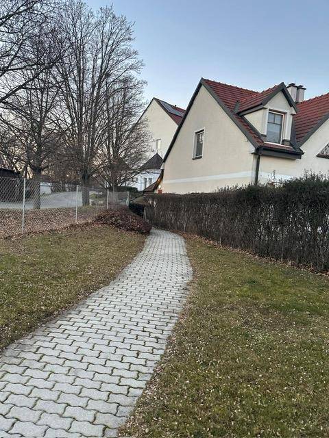 Gepflasterter Weg führt zu einem Wohngebäude mit traditioneller Architektur und gepflegten Hecken.
