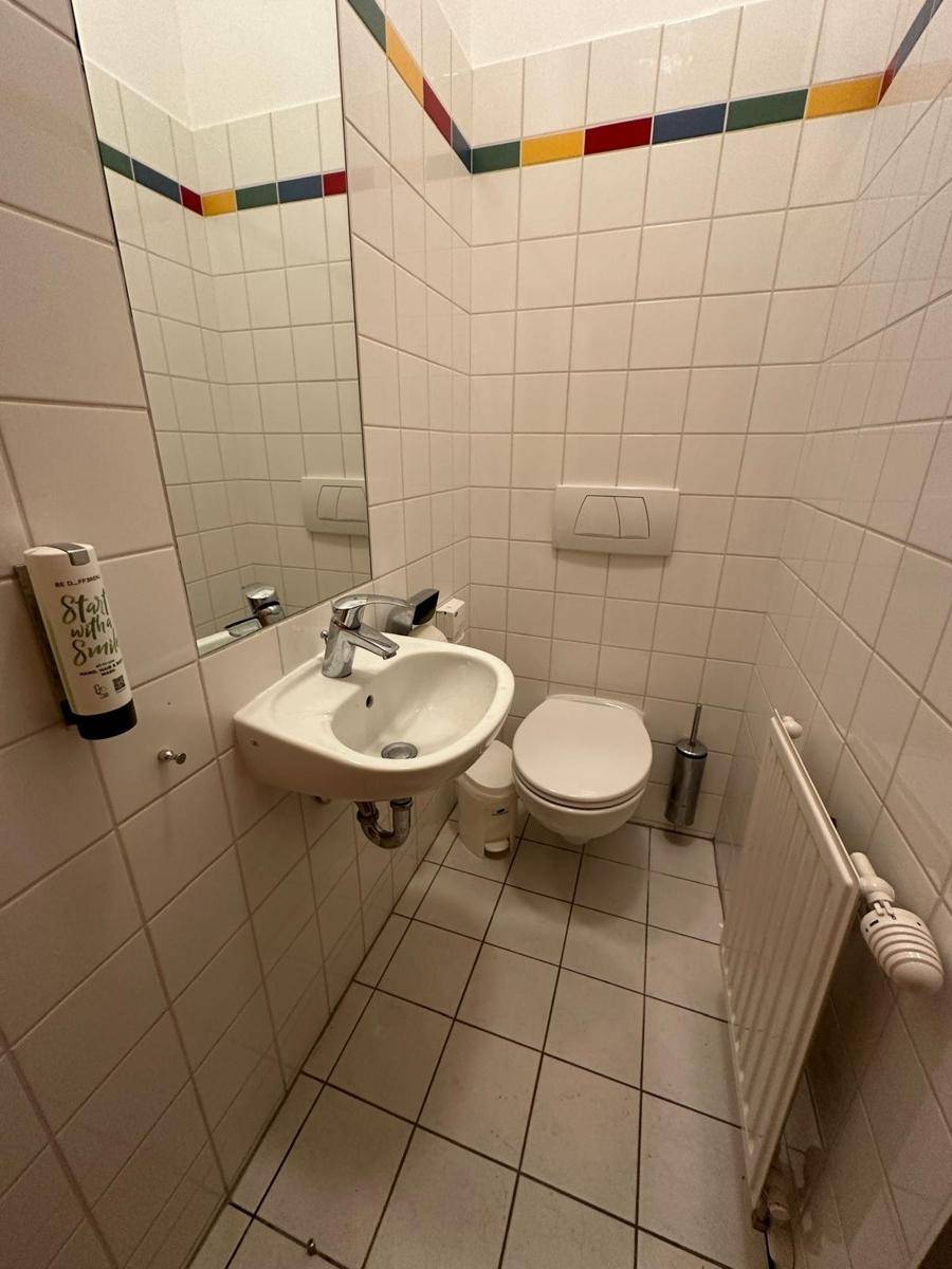 Kleines Gäste-WC mit weißen Fliesen, Waschbecken und wandhängender Toilette.