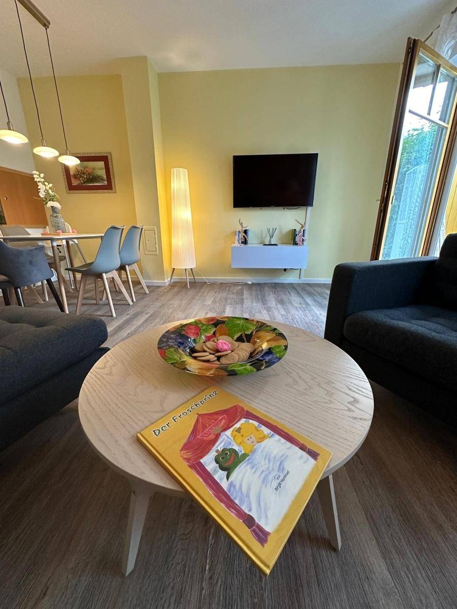 Wohnzimmer mit Couchtisch, Fernseher an der Wand und einem Kinderbuch als charmante Dekoration.