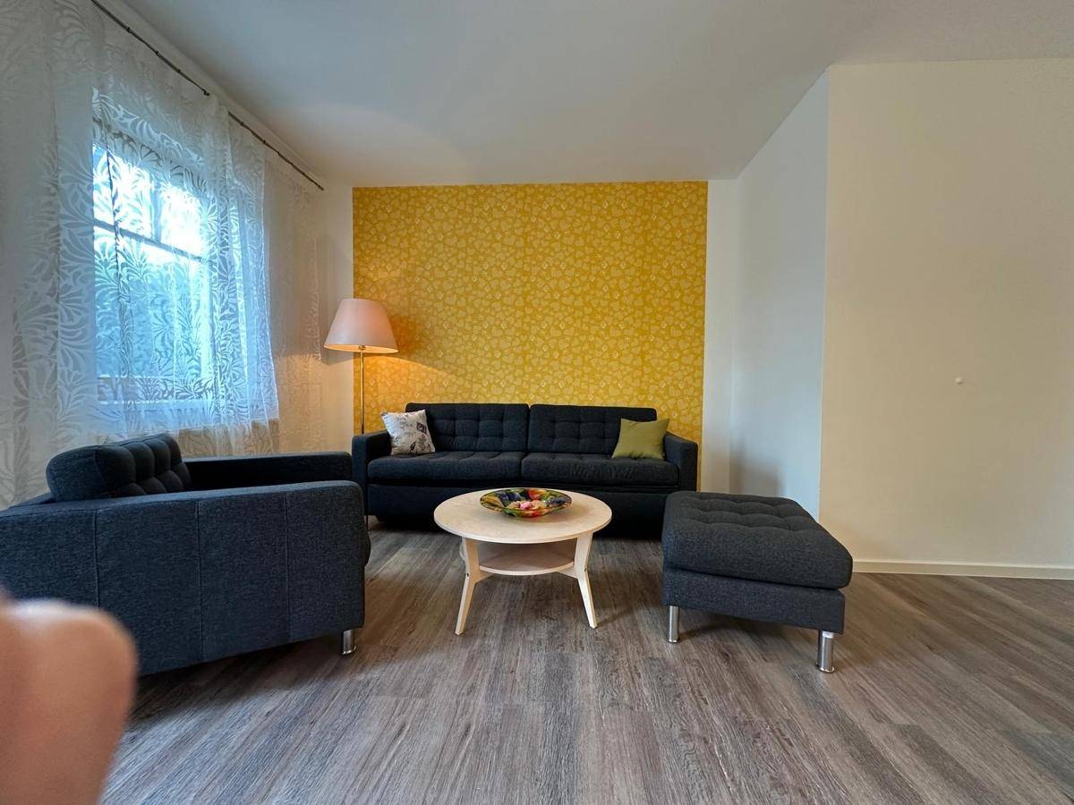 Gemütliches Wohnzimmer mit dunklem Sofa, Couchtisch und einer auffälligen gelben Akzentwand.