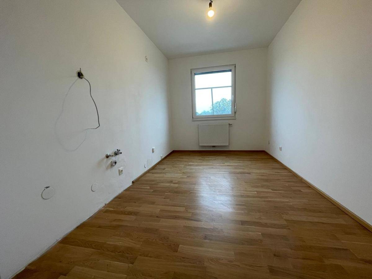 Leeres Zimmer mit Parkettboden und einem Fenster, vorbereitet für Installationen an der Wand.