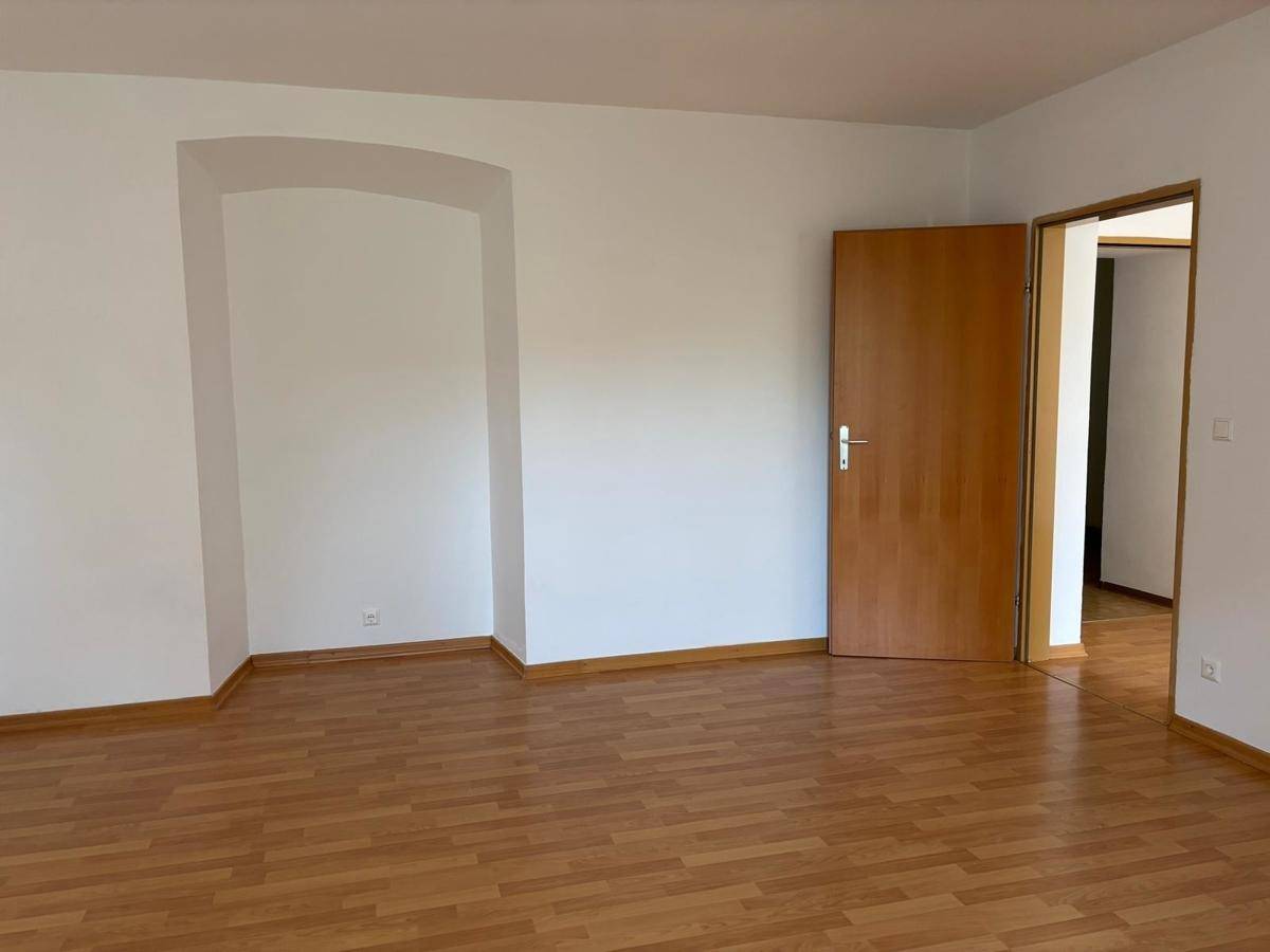 Leeres Zimmer mit Laminatboden, Holztür und einer dekorativen Nische in der Wand.