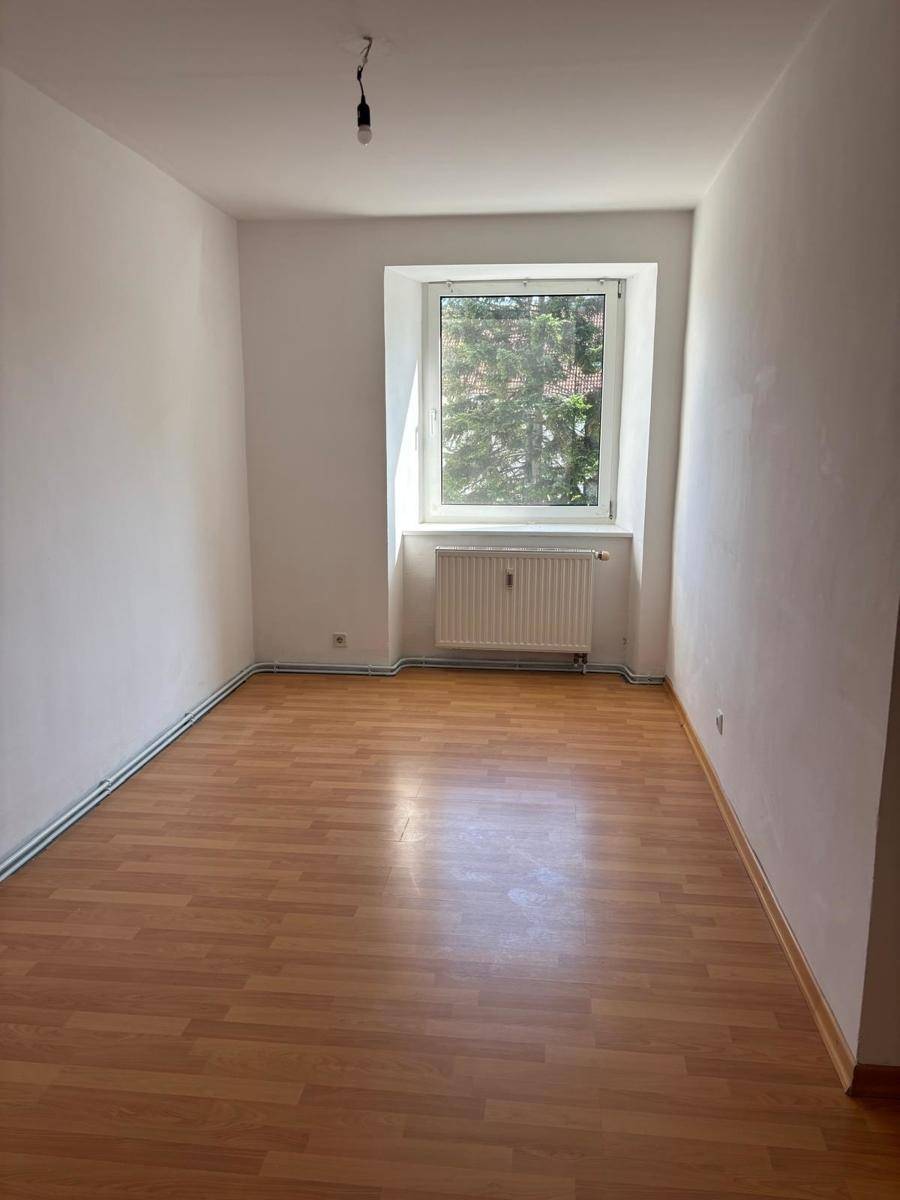 Leeres Zimmer mit Laminatboden und Fenster, das viel Tageslicht hereinlässt.