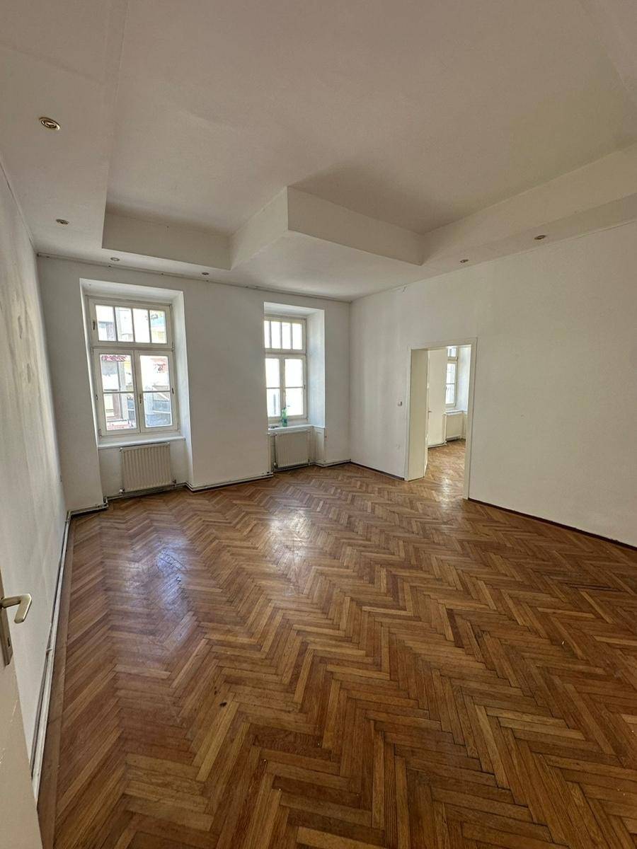 Helles Wohnzimmer mit Fischgrätparkett, hohen Fenstern und indirekter Deckenbeleuchtung.
