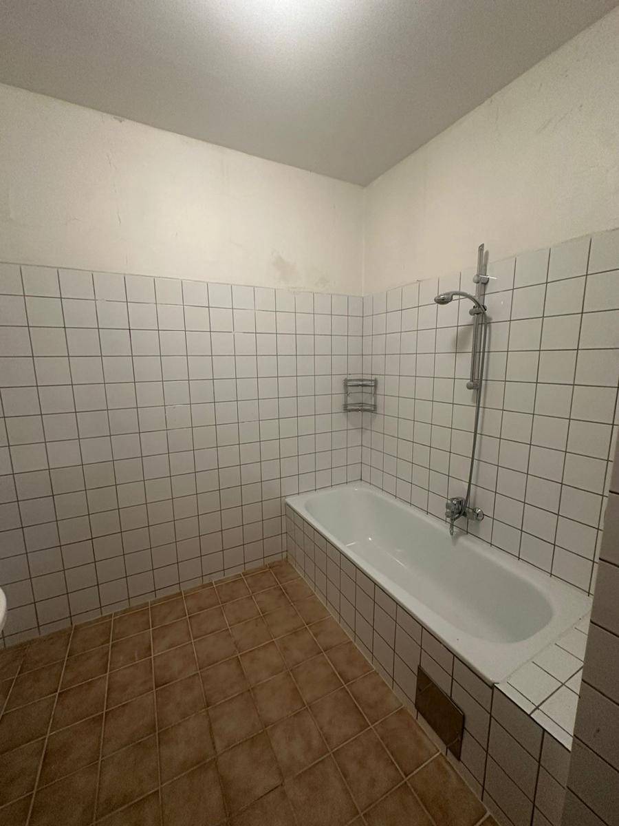 Badezimmer mit Badewanne und weißen Wandfliesen, bereit zur Modernisierung.