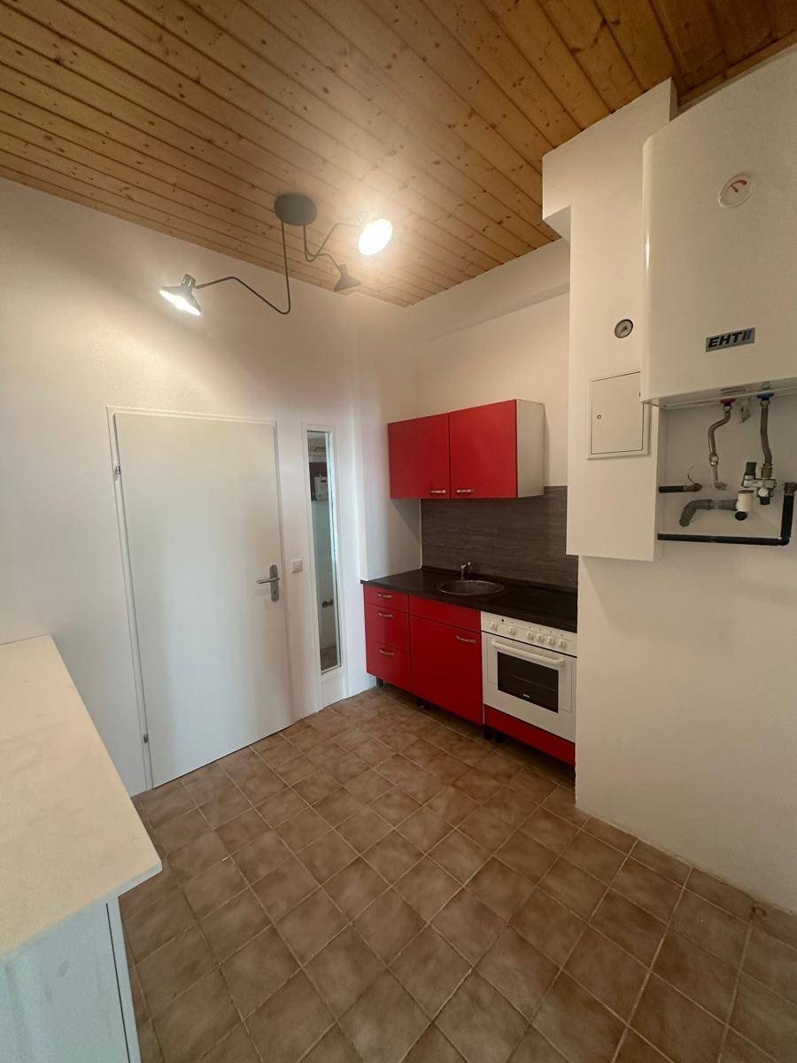Funktionale Küchenzeile mit roten Schränken und Holzdecke in einem hellen Raum.