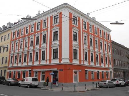 Mehrstöckiges Gebäude an einer Straßenecke mit auffälliger orange-weißer Fassade und vielen Fenstern.