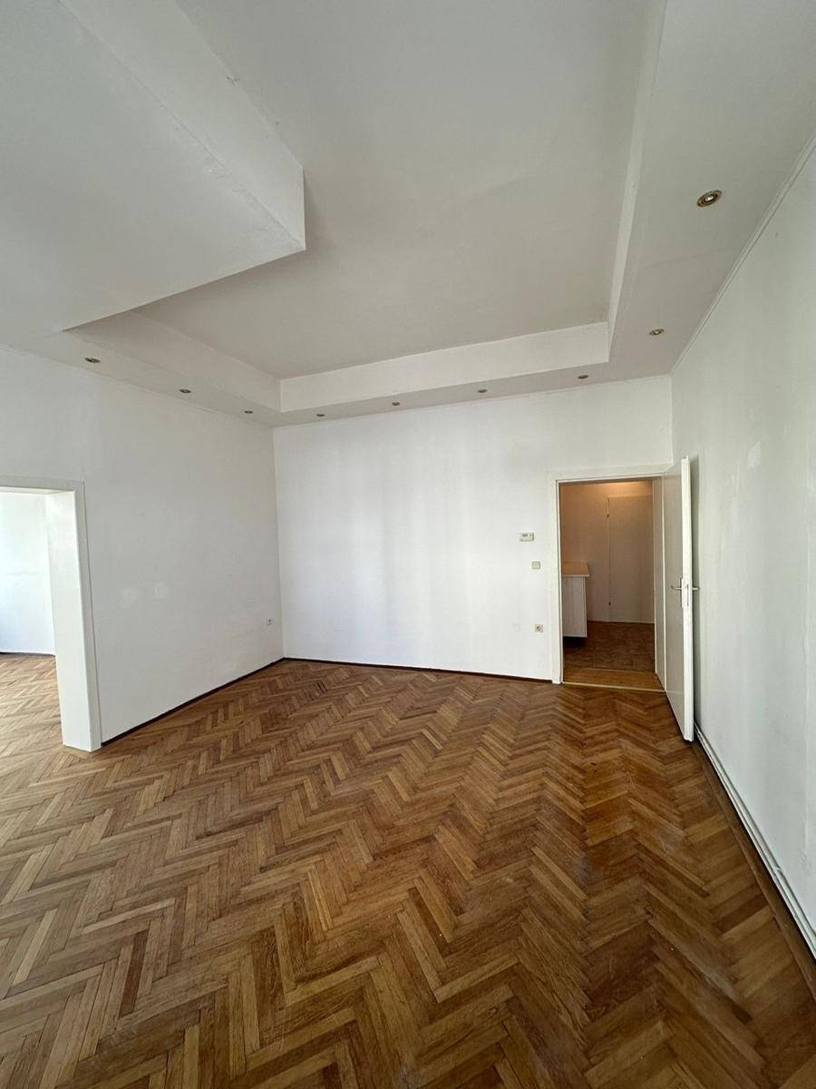 Geräumiges Wohnzimmer mit Fischgrätparkett und moderner Deckenbeleuchtung.