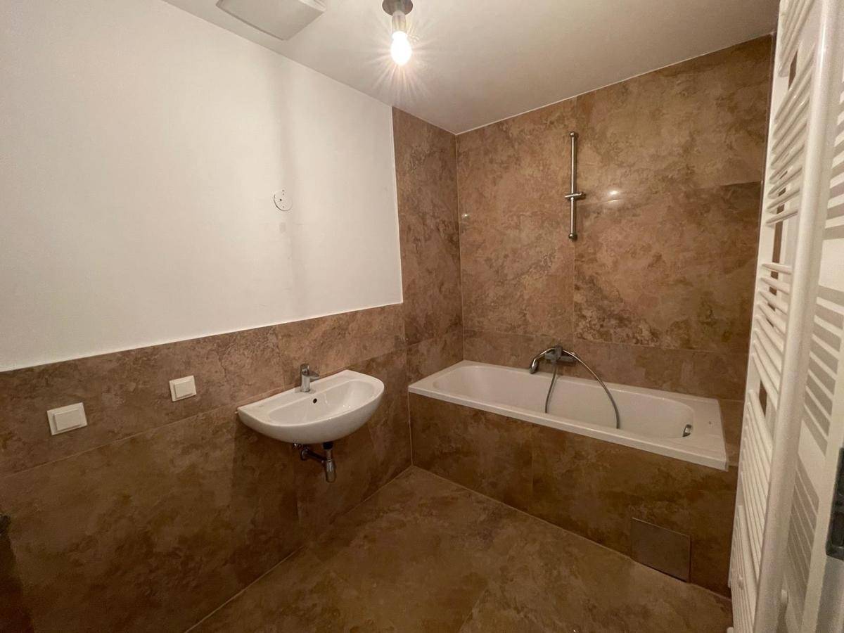 Modernes Badezimmer mit braunen Fliesen, Badewanne, Waschbecken und einem praktischen Handtuchheizkörper.