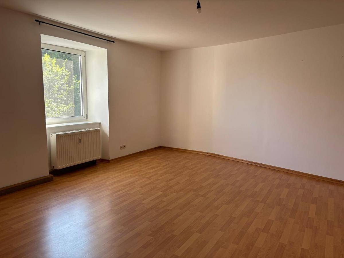 Geräumiges, leeres Zimmer mit Laminatboden und einem Fenster, das den Raum erhellt.