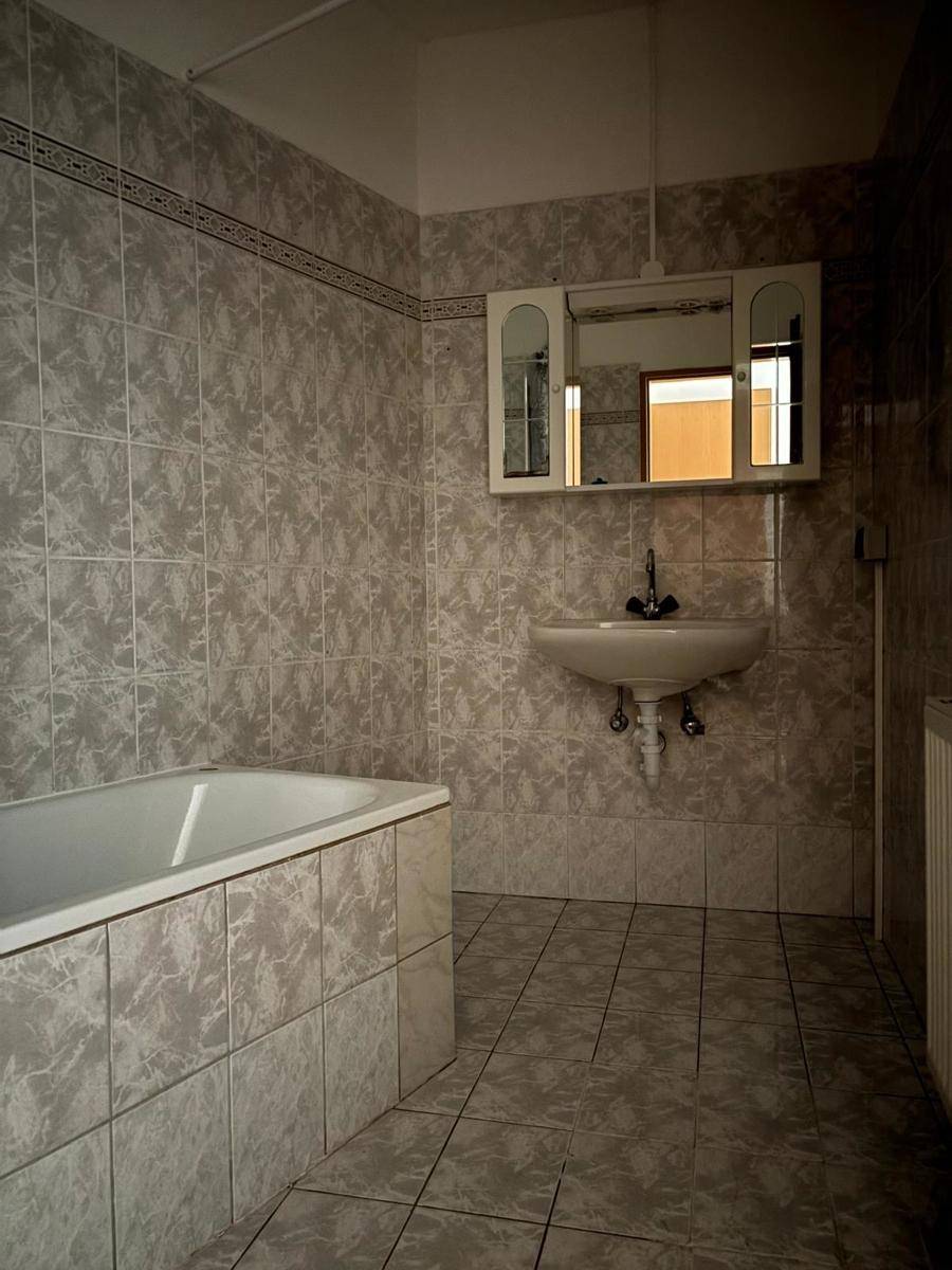 Badezimmer mit Badewanne, Waschbecken und Spiegelschrank, komplett gefliest in Grau.