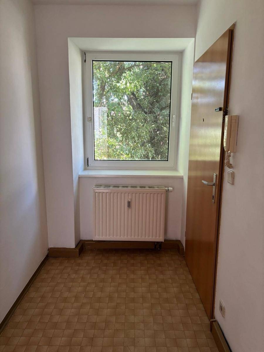 Eingangsbereich mit Fenster, Heizkörper und Blick ins Grüne, einfacher Vinylboden.