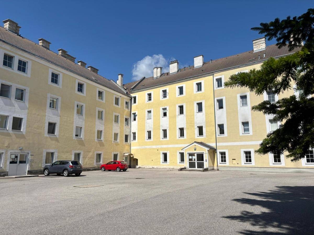 Großer Innenhof eines historischen Gebäudekomplexes mit Parkplätzen und Bäumen.