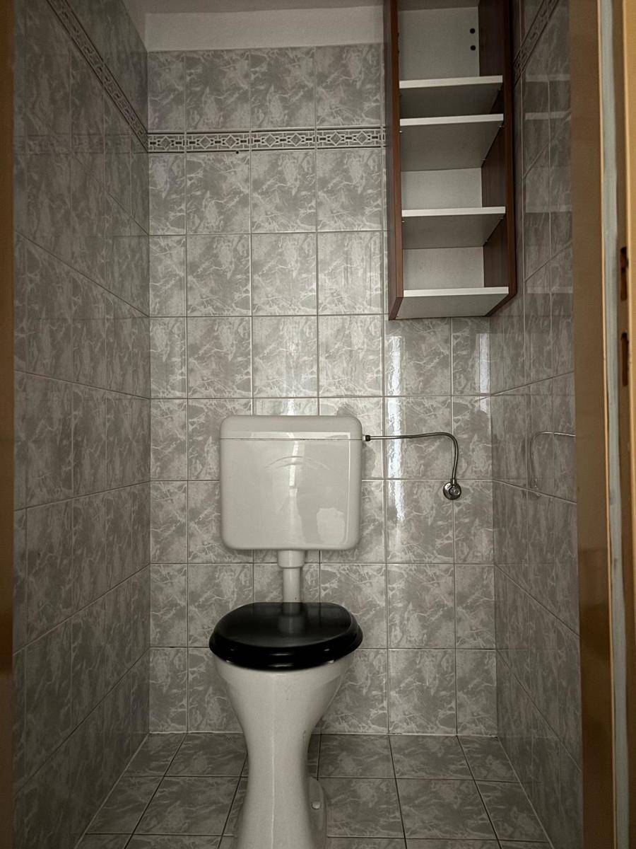 Kleines separates WC mit grauen Fliesen an Wänden und Boden, einfach ausgestattet.