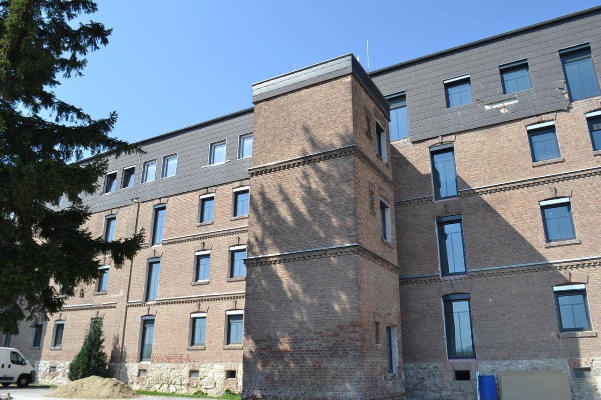 Historisches Backsteingebäude mit vielen Fenstern und einem modernisierten Dachbereich unter blauem Himmel.