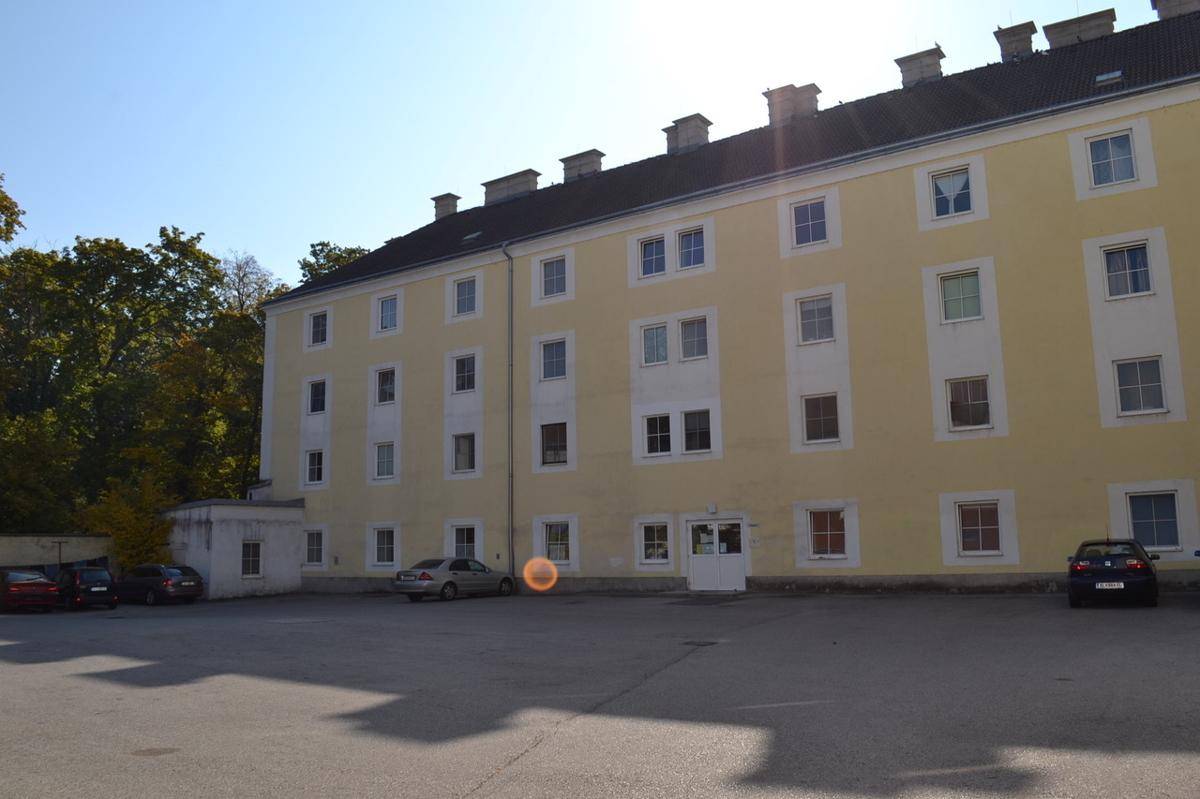 Rückseite eines historischen Gebäudes mit großem Parkplatz und Eingangsbereich.