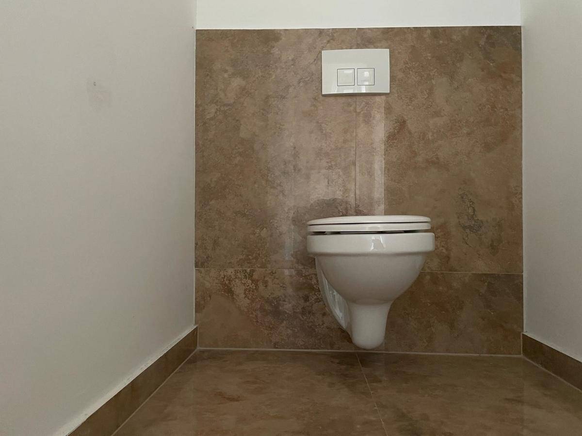Separate Toilette mit Wand-WC und braunen Fliesen an Wand und Boden, sauber und funktional.