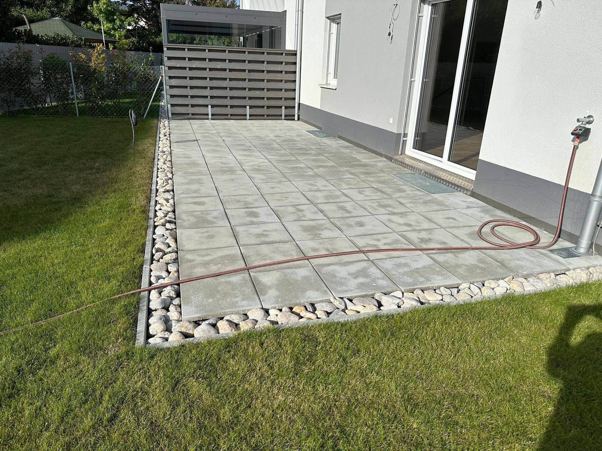 Gepflasterte Terrasse neben einem grünen Rasenbereich, bereit für die Gartengestaltung.