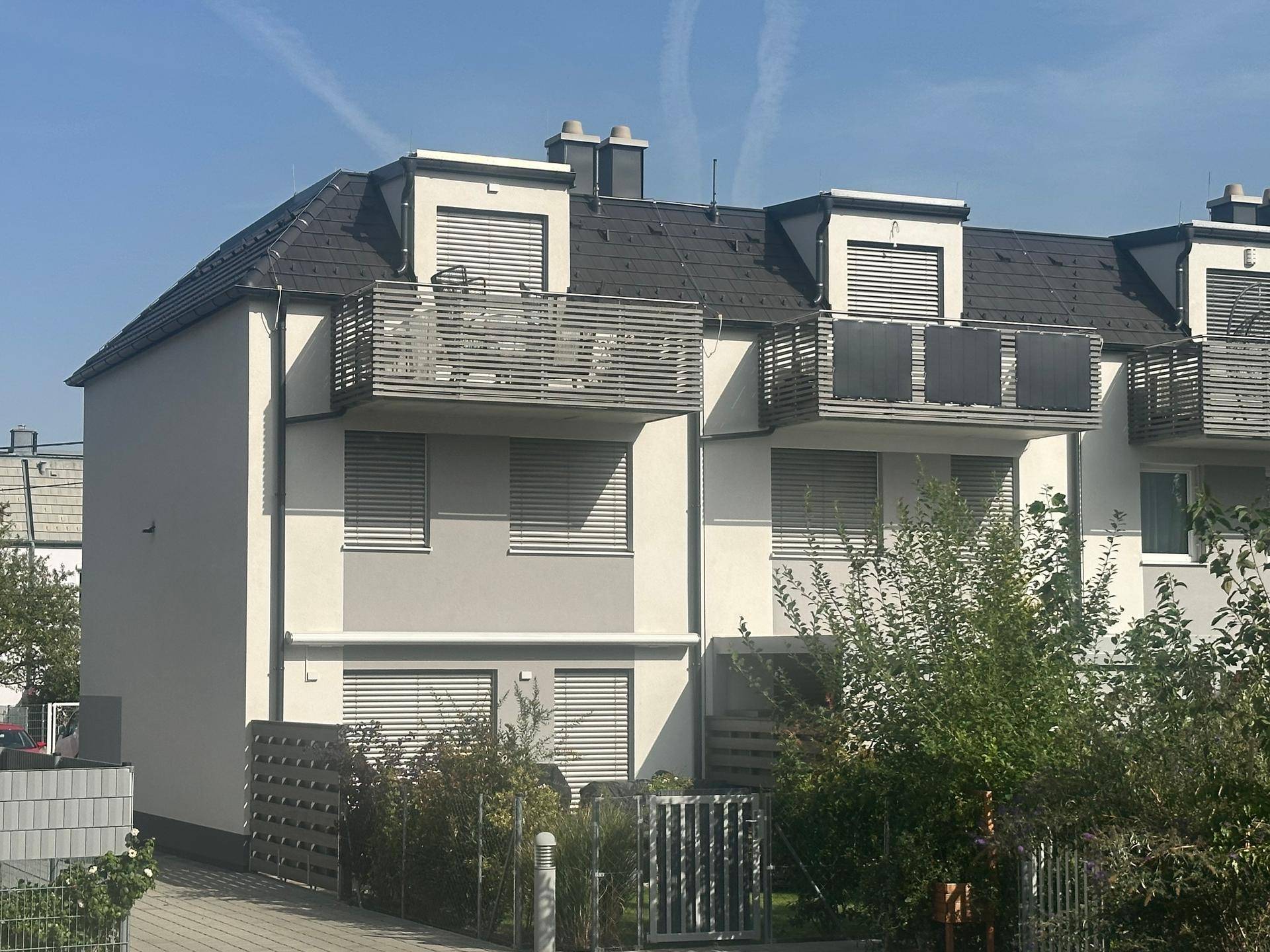 Reihenhäuser mit moderner Architektur, Balkonen und Rollläden unter klarem Himmel.