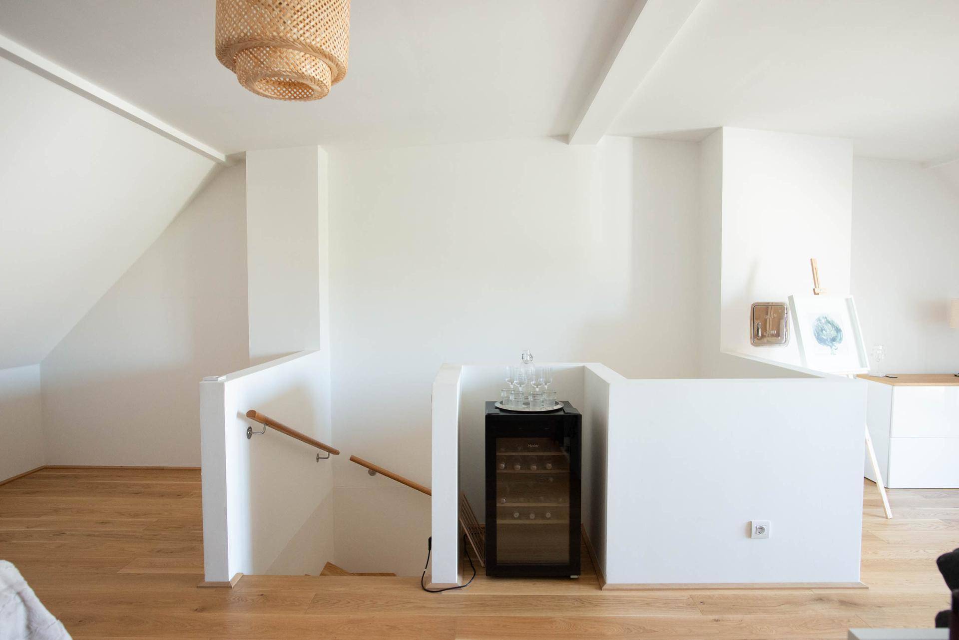 Heller Flurbereich im Obergeschoss mit Holztreppe, Geländer und integriertem Weinkühlschrank.