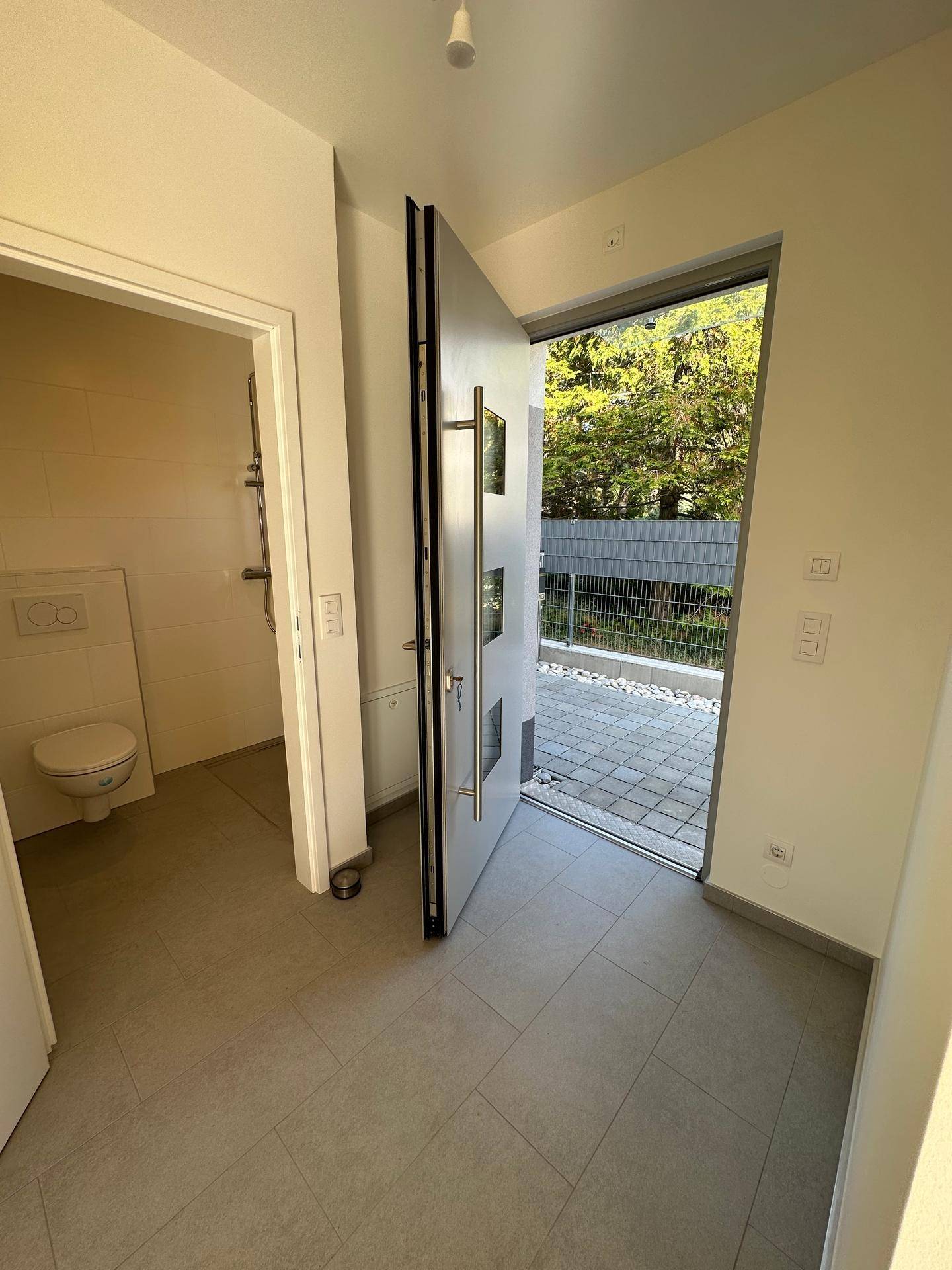 Heller Eingangsbereich mit offener Tür, Blick nach draußen und Zugang zu einem Gäste-WC.