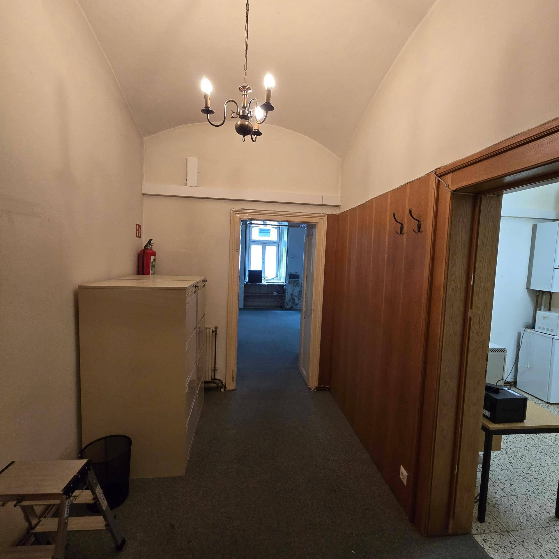 Langer Flur mit Teppichboden, Holzverkleidung an der Wand und einem klassischen Kronleuchter an der gewölbten Decke.
