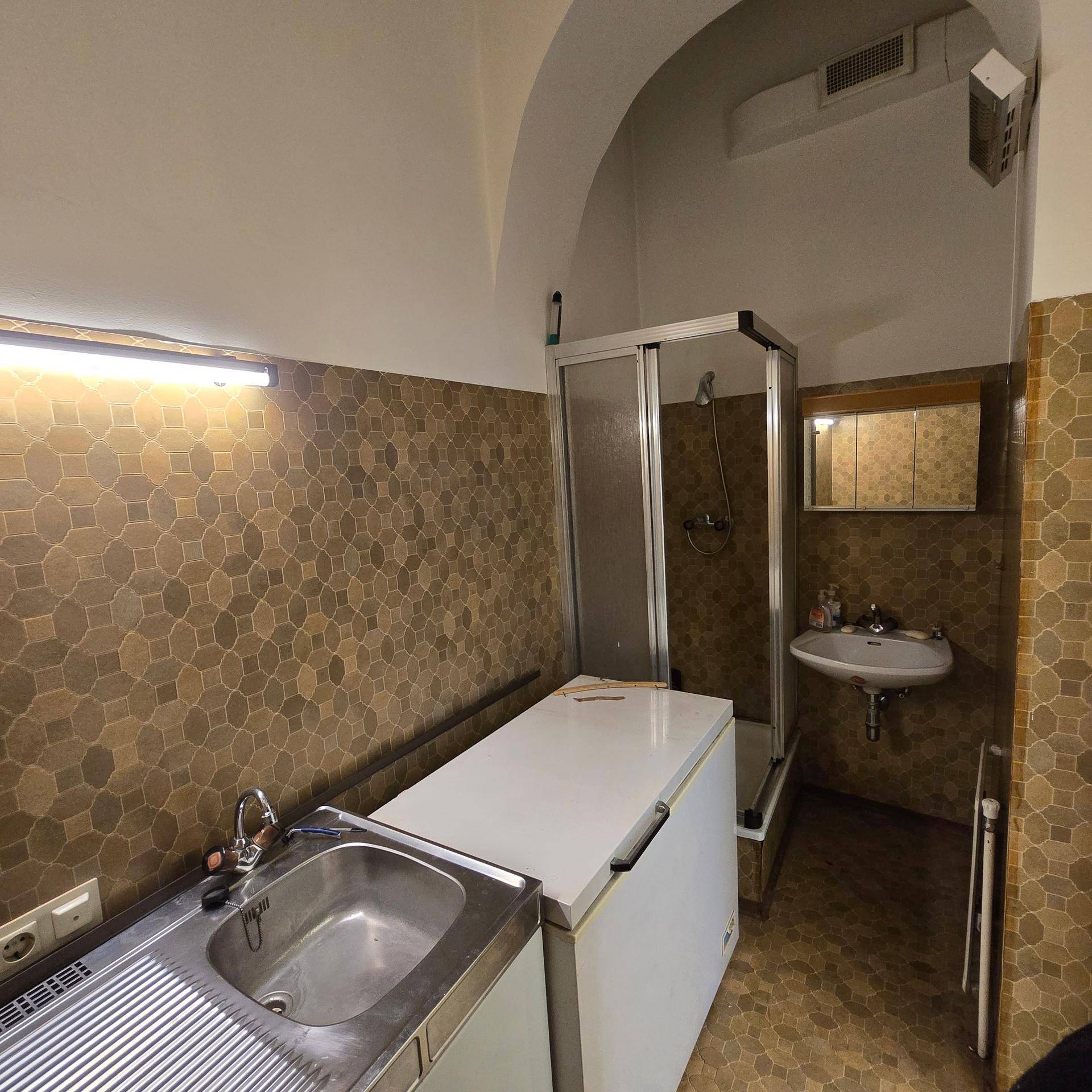 Badezimmer mit Duschkabine, Waschbecken, Fliesenboden und gemusterten Wandfliesen in Brauntönen.
