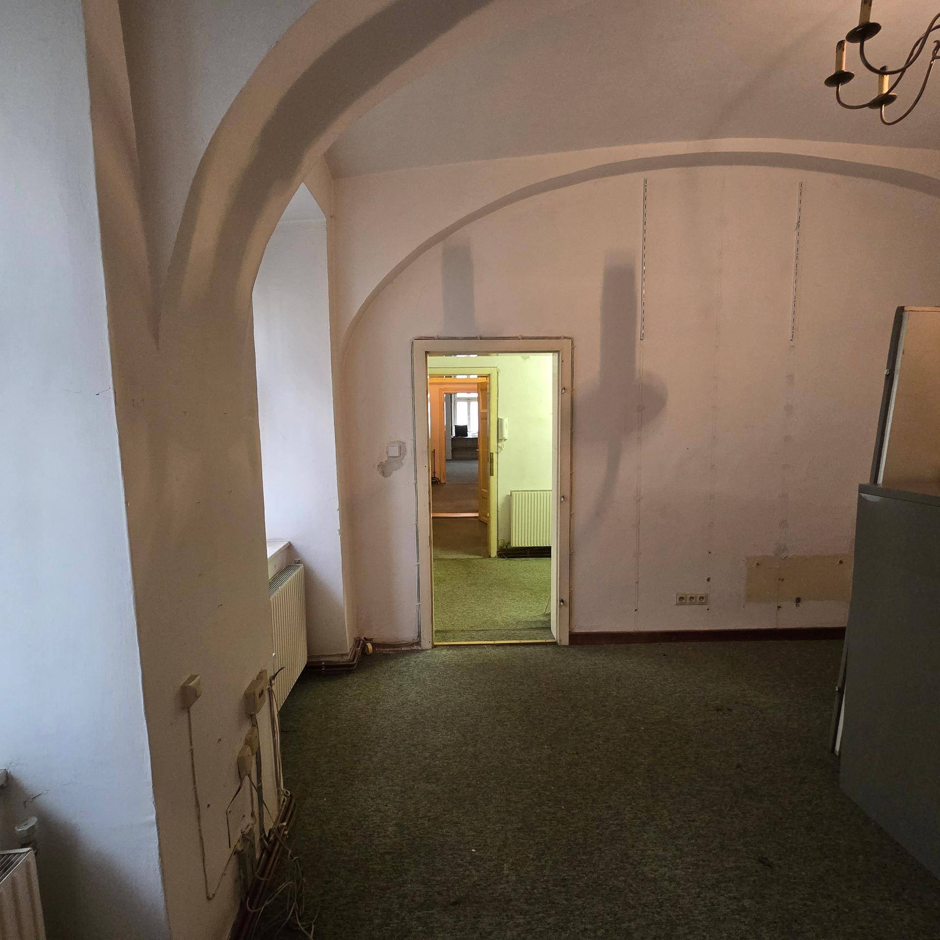 Büroraum mit Teppichboden, gewölbter Decke und Blick durch eine Tür in einen weiteren Raum, in gutem Zustand.