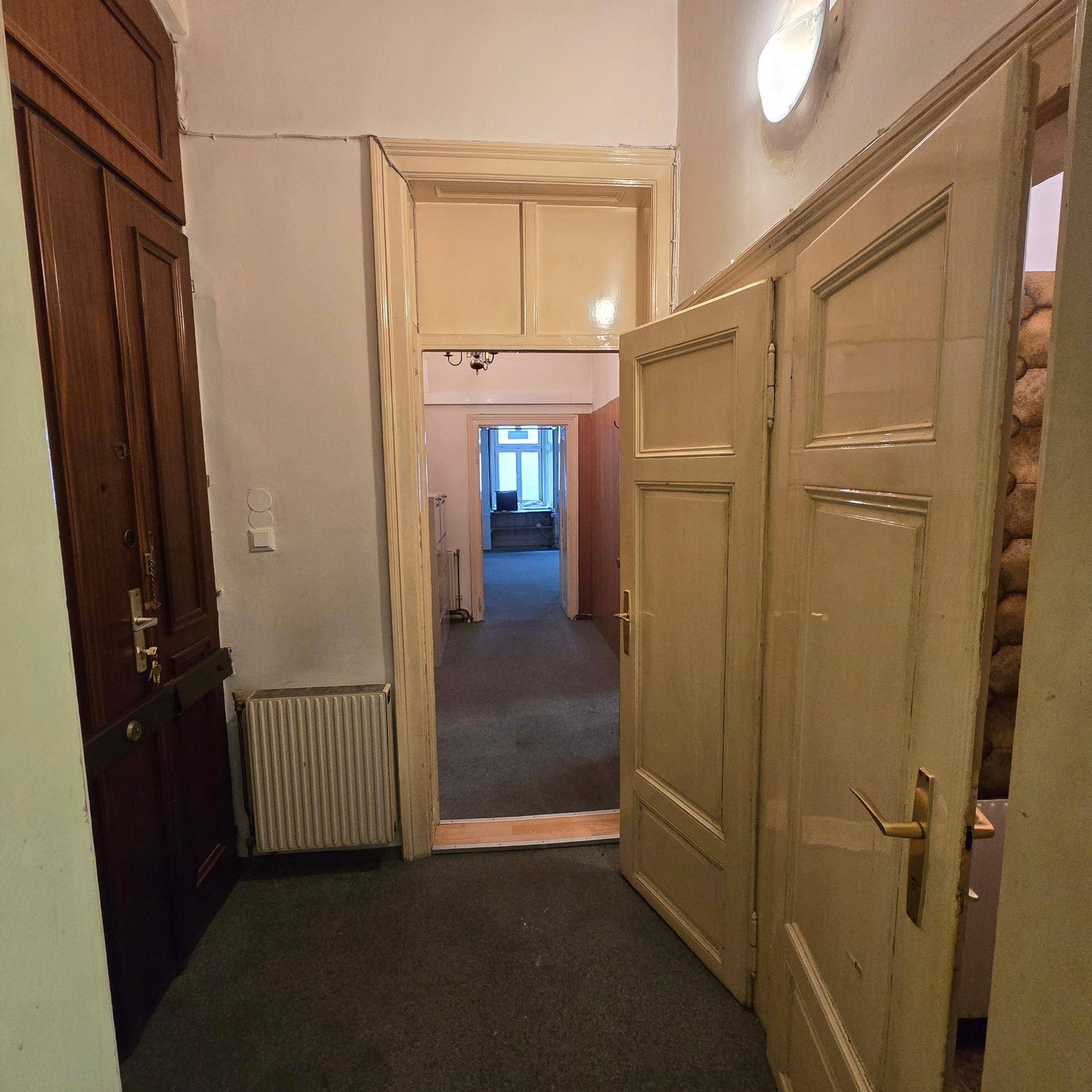 Flur mit Teppichboden, mehreren traditionellen Türen und Blick in einen helleren Raum, in gutem Zustand.
