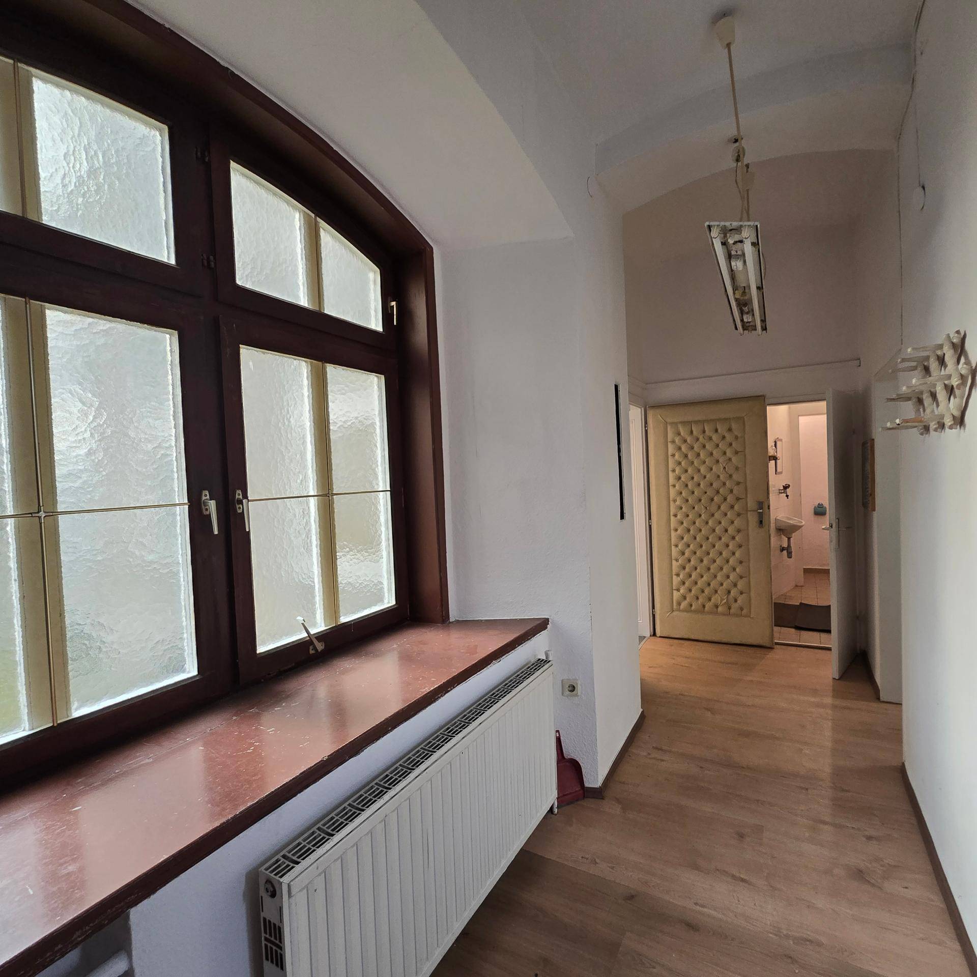Flur mit Laminatboden, einem großen Fenster mit Milchglas und Blick auf eine traditionelle Tür.